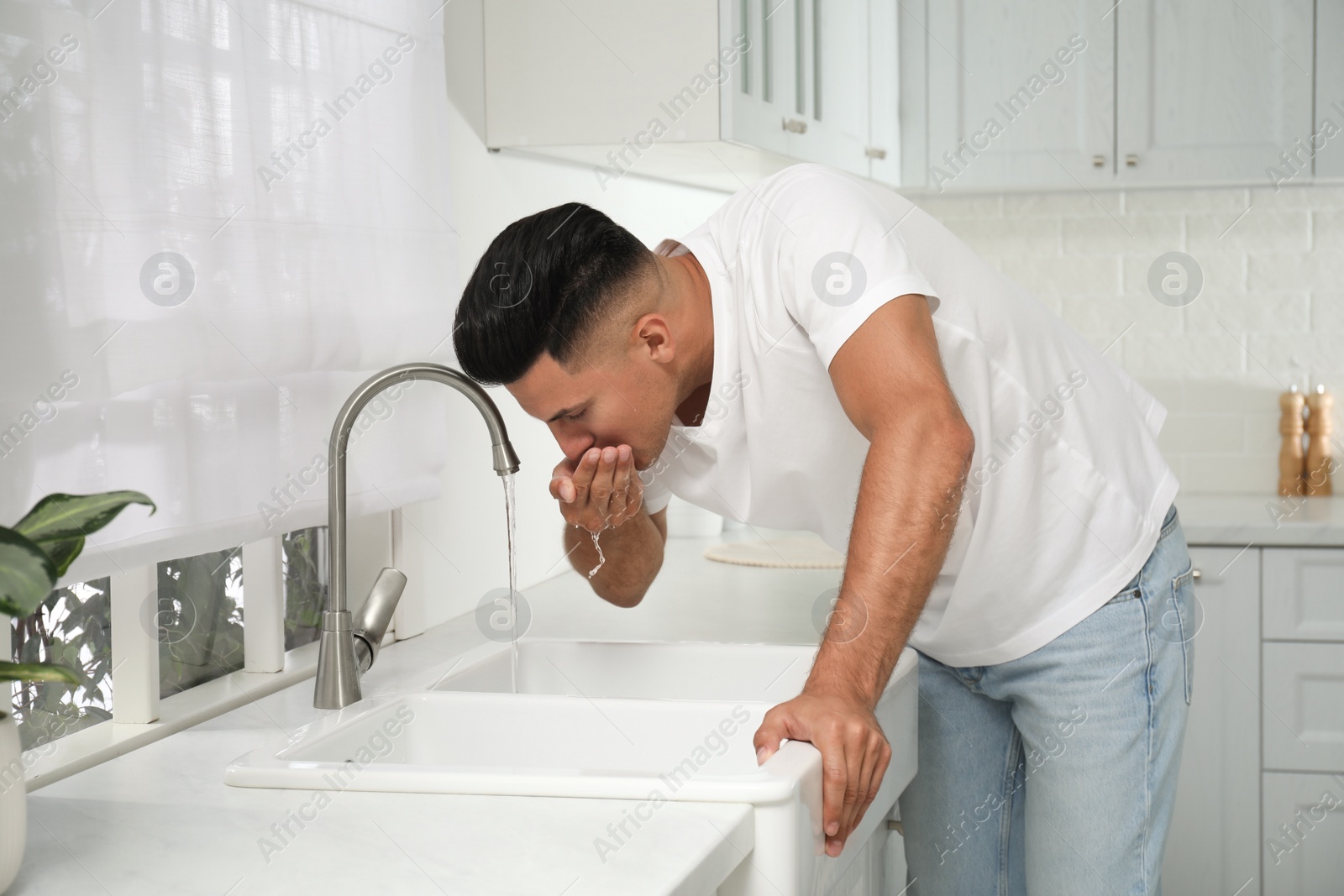 Photo of Man drinking tap water over sink in kitchen