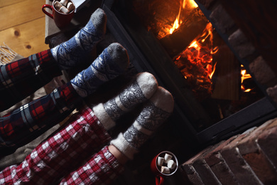 Photo of Couple in pajamas resting near fireplace indoors, closeup. Winter vacation