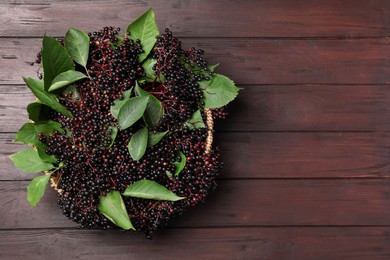 Ripe elderberries with green leaves on wooden table, top view. Space for text