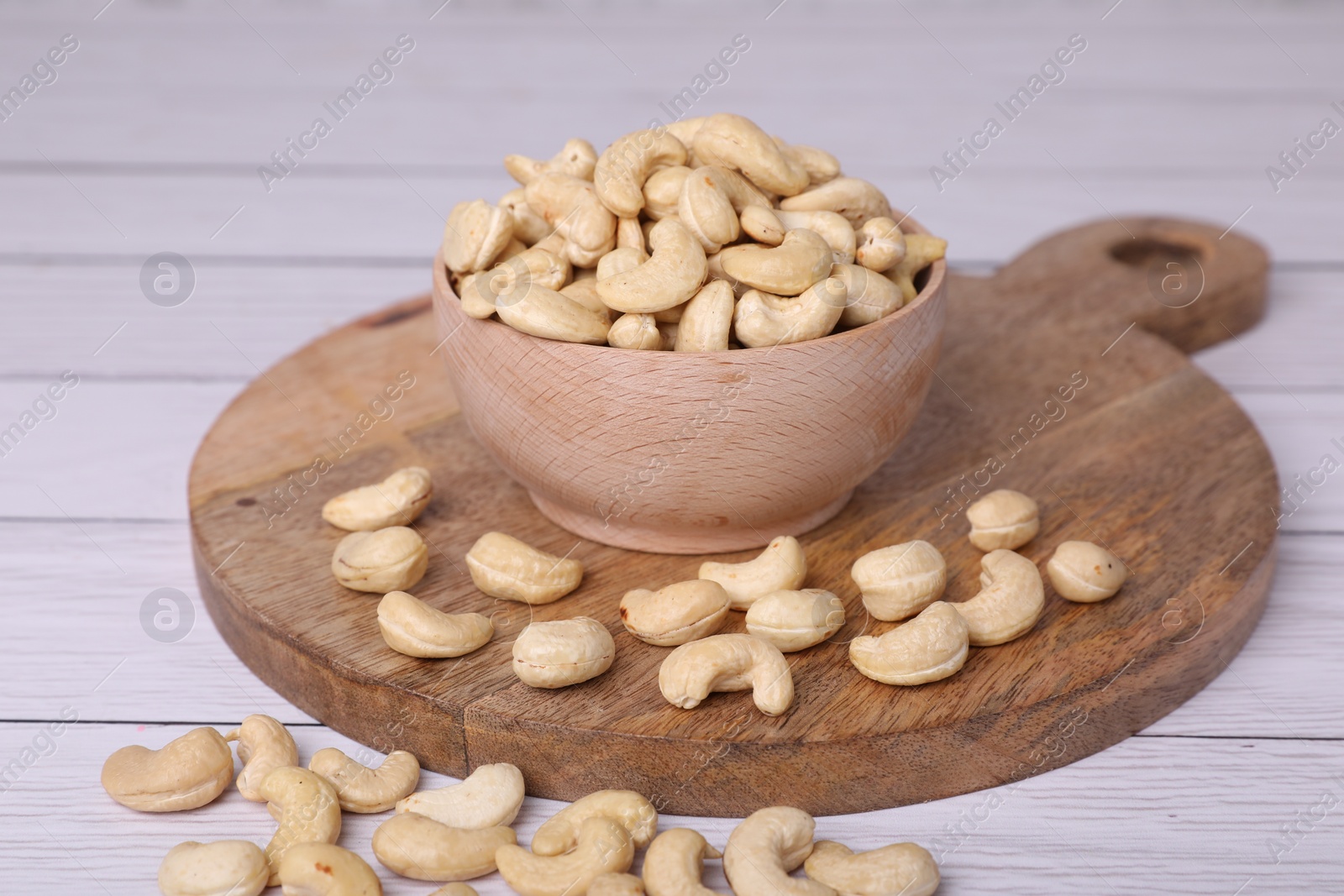 Photo of Tasty cashew nuts in bowl on white wooden table