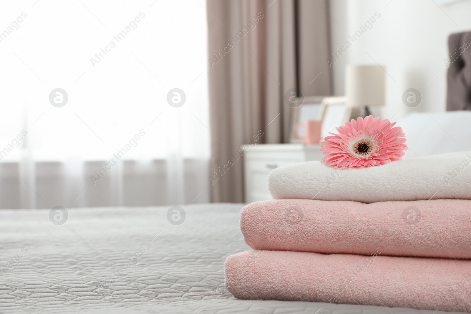 Photo of Stack of clean towels with flower on bed indoors. Space for text