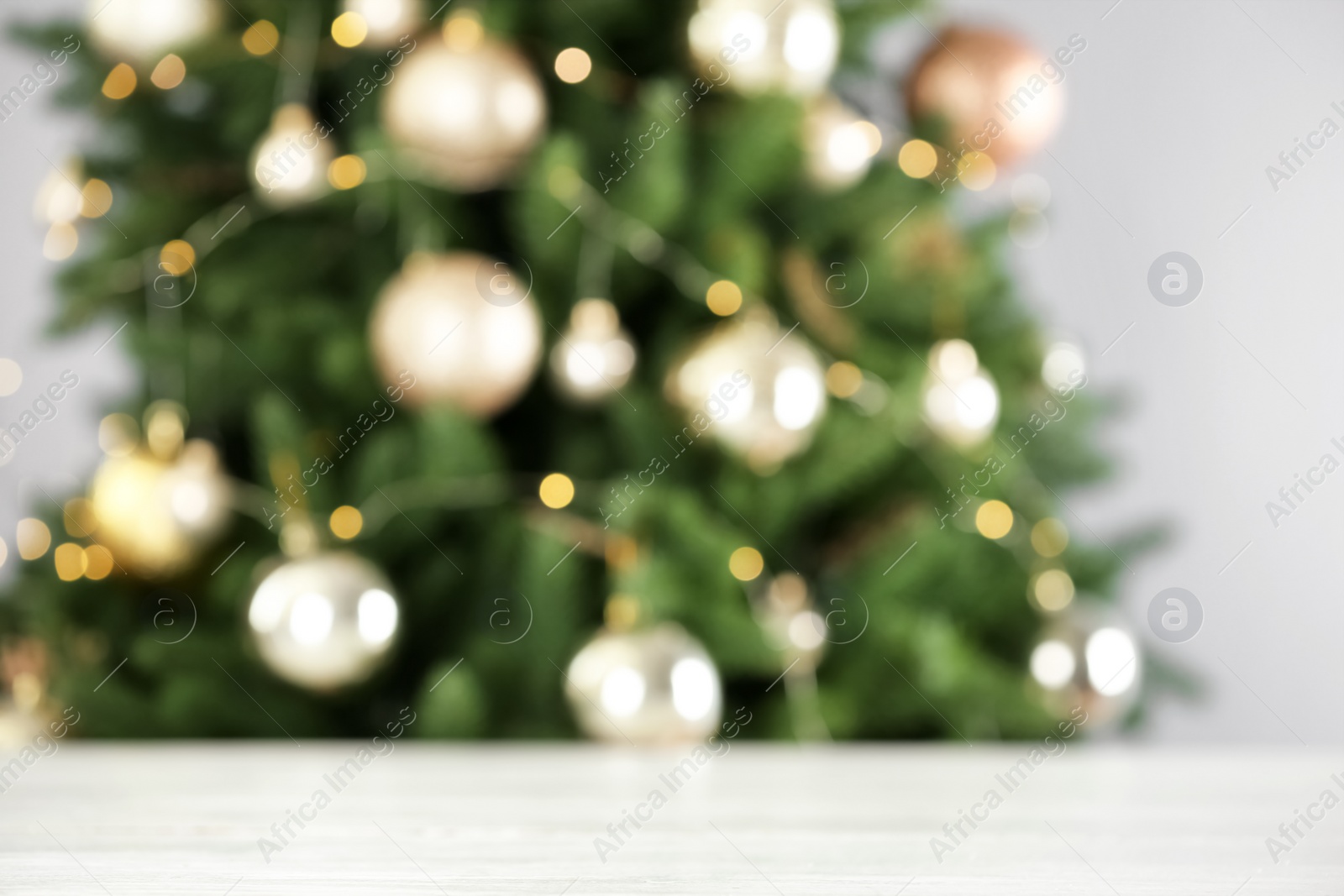 Photo of Empty white wooden table and blurred fir tree with Christmas lights on background, bokeh effect. Space for design