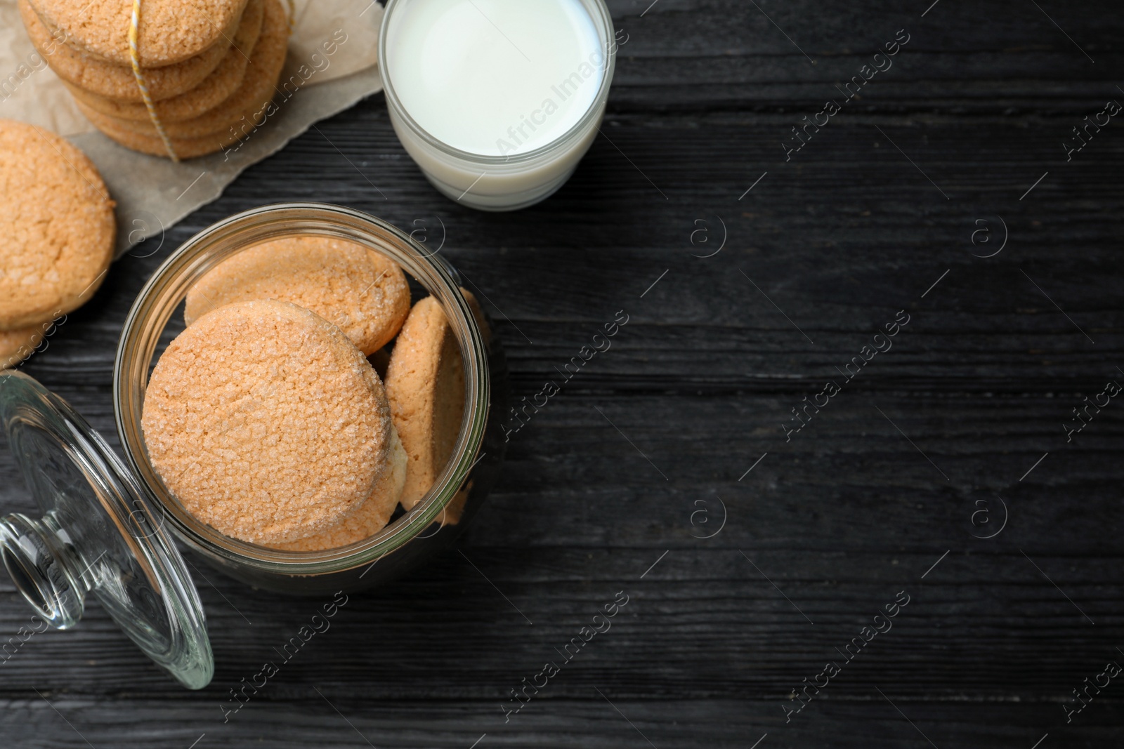 Photo of Delicious sugar cookies and glass of milk on black wooden table, flat lay. Space for text