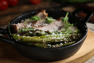 Photo of Tasty meat served with asparagus and sprouts in portioned frying pan on table, closeup