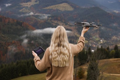 Photo of Young woman with modern drone in mountains, back view