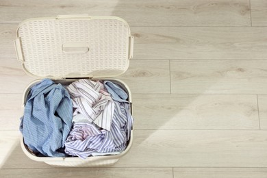 Photo of Laundry basket with clothes on floor, top view. Space for text