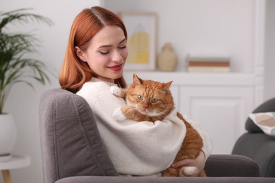 Woman with her cute cat in armchair at home