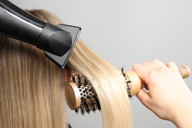 Photo of Hairdresser blow drying client's hair on light grey background, closeup