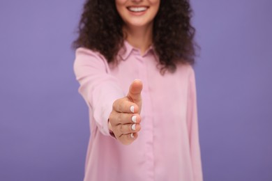Woman welcoming and offering handshake on violet background, closeup