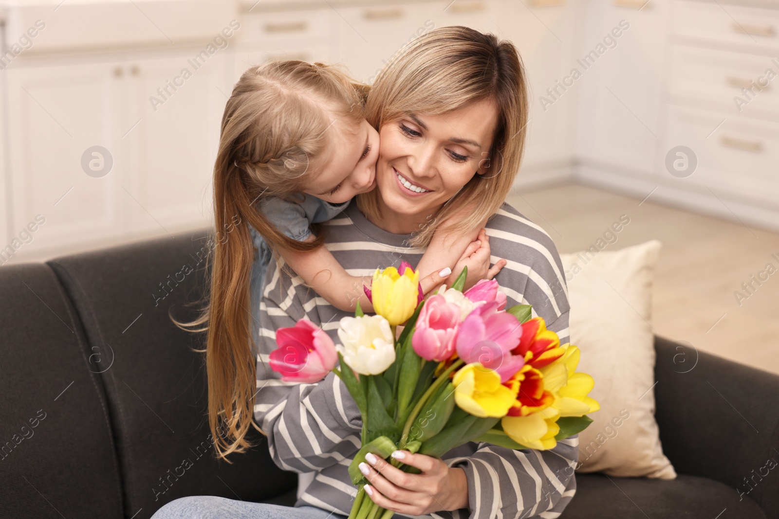 Photo of Little daughter kissing and congratulating her mom with Mother`s Day at home. Woman holding bouquet of beautiful tulips