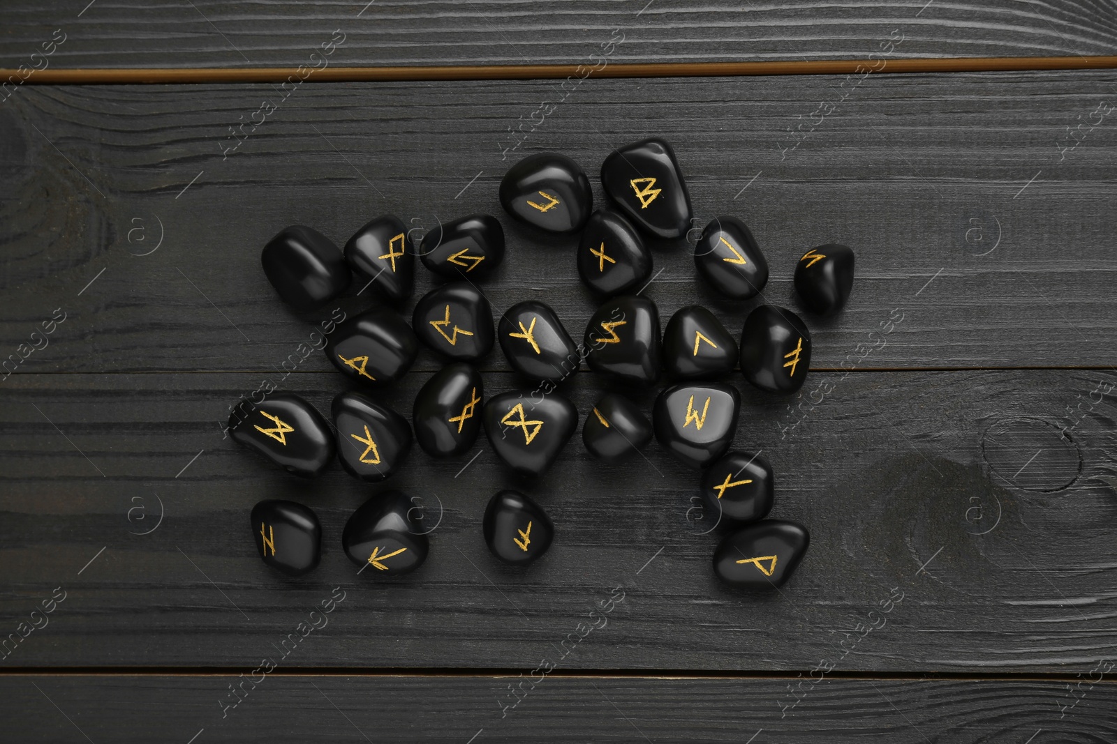 Photo of Pile of rune stones on black wooden table, flat lay