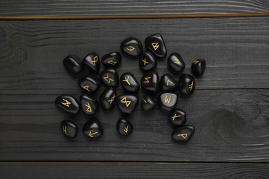 Photo of Pile of rune stones on black wooden table, flat lay