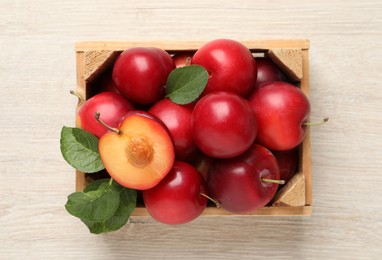 Photo of Delicious ripe cherry plums with leaves on white wooden table, top view