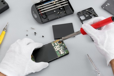 Technician repairing broken smartphone at table, closeup