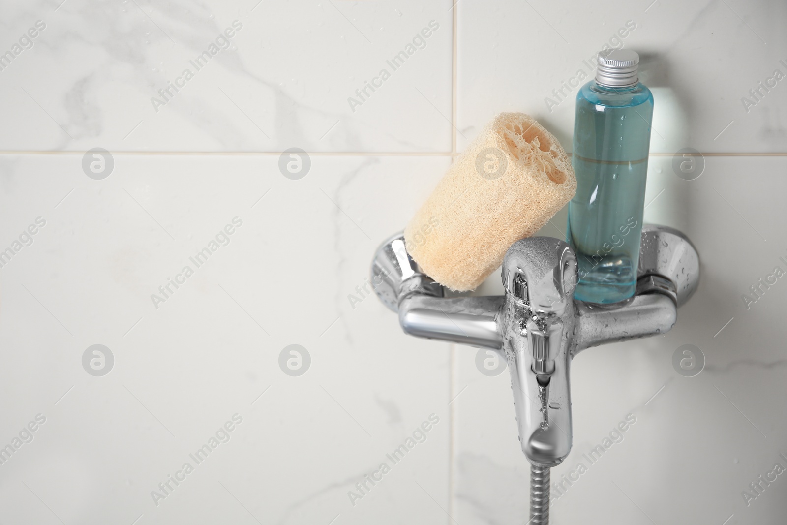 Photo of Natural loofah sponge and shower gel bottle on faucet in bathroom, space for text