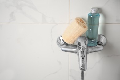 Natural loofah sponge and shower gel bottle on faucet in bathroom, space for text