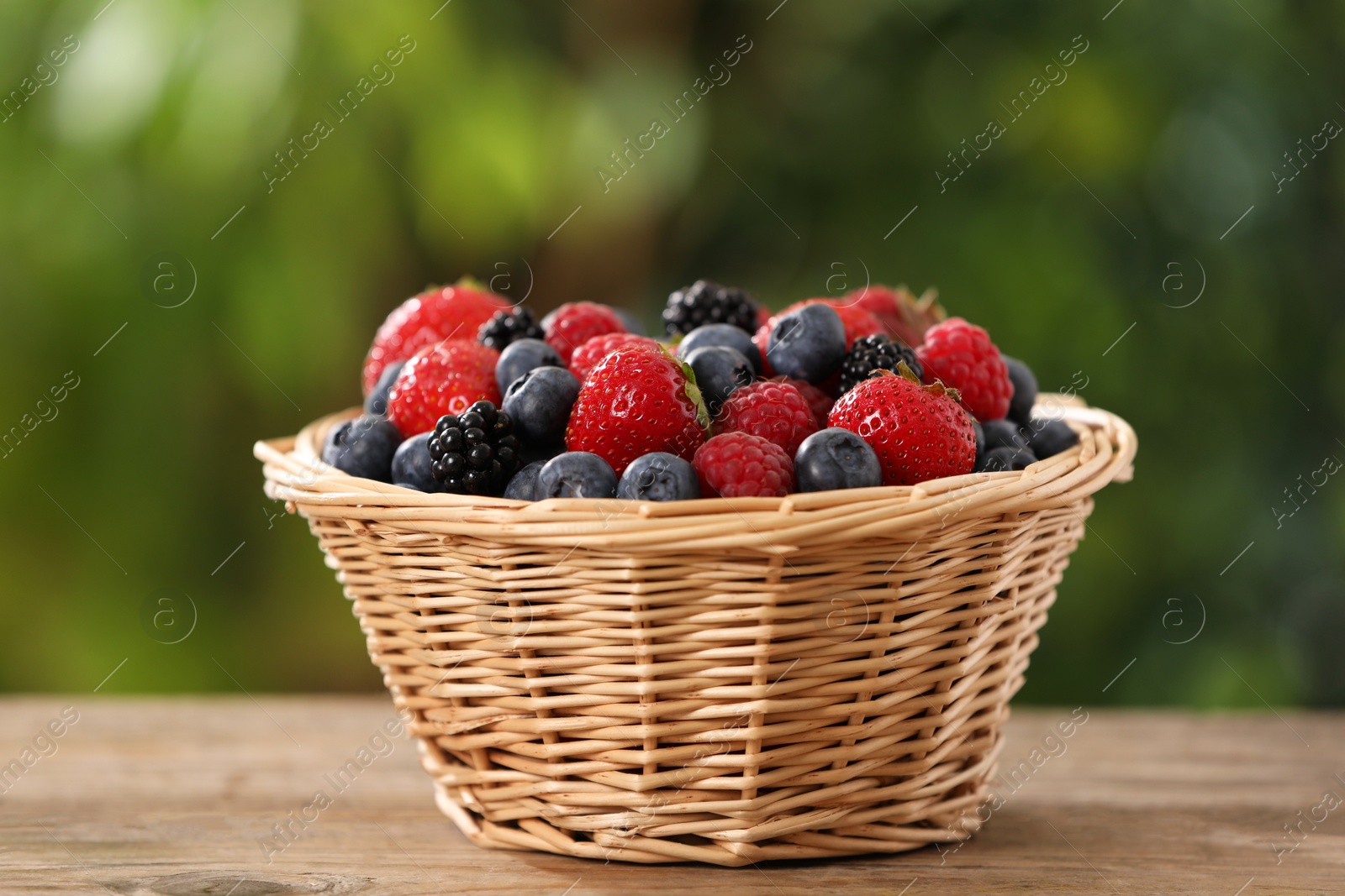 Wicker bowl with different fresh ripe berries on wooden table outdoors Photo of Wicker bowl with different fresh ripe berries on wooden table outdoors