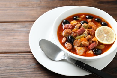 Photo of Meat solyanka soup with sausages, olives, vegetables and spoon on wooden table, space for text