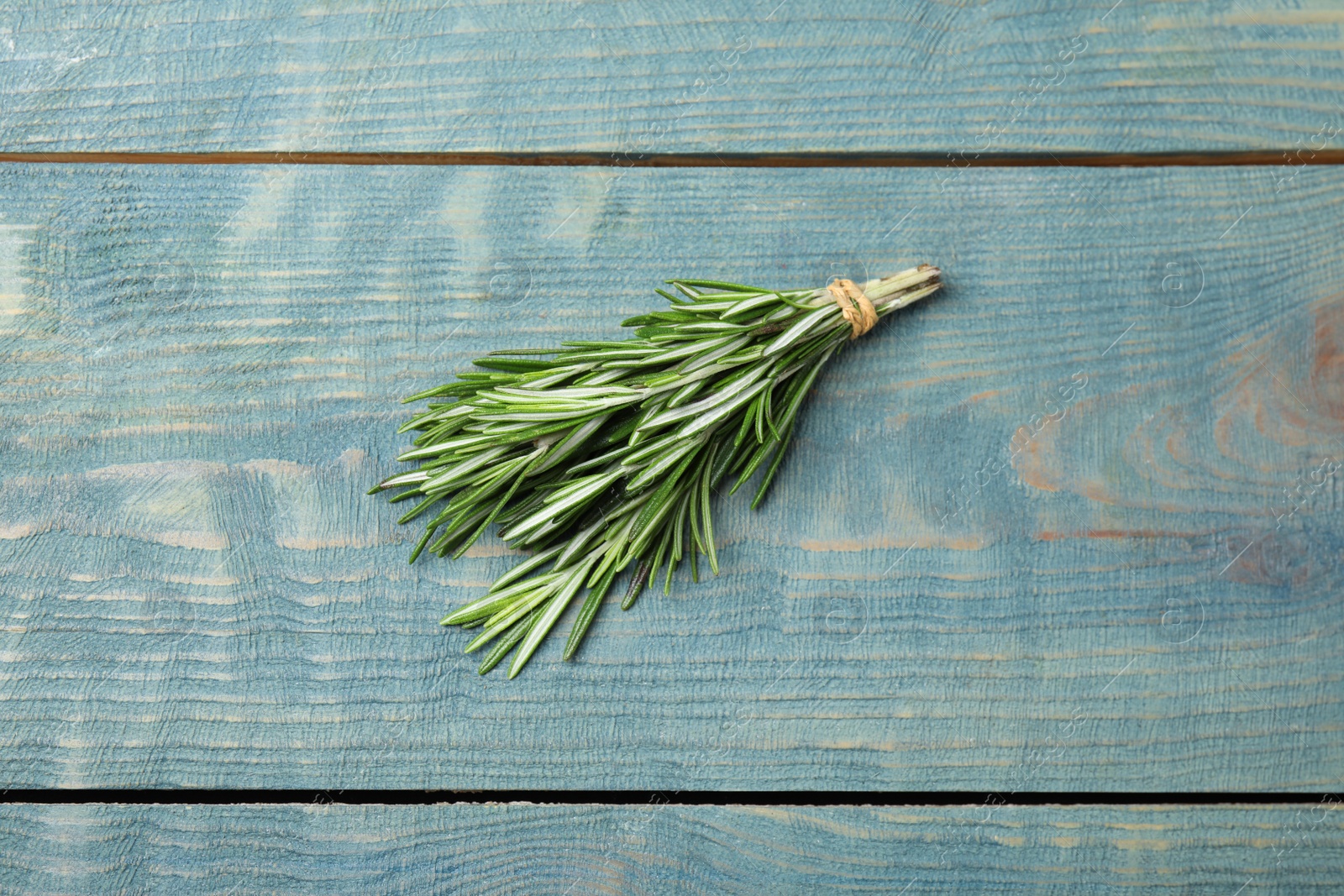 Photo of Bunch of fresh rosemary on blue wooden table, above view