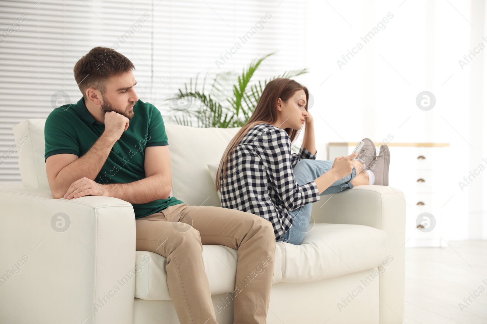 Photo of Young man peering into girlfriend's smartphone at home. Relationship problems