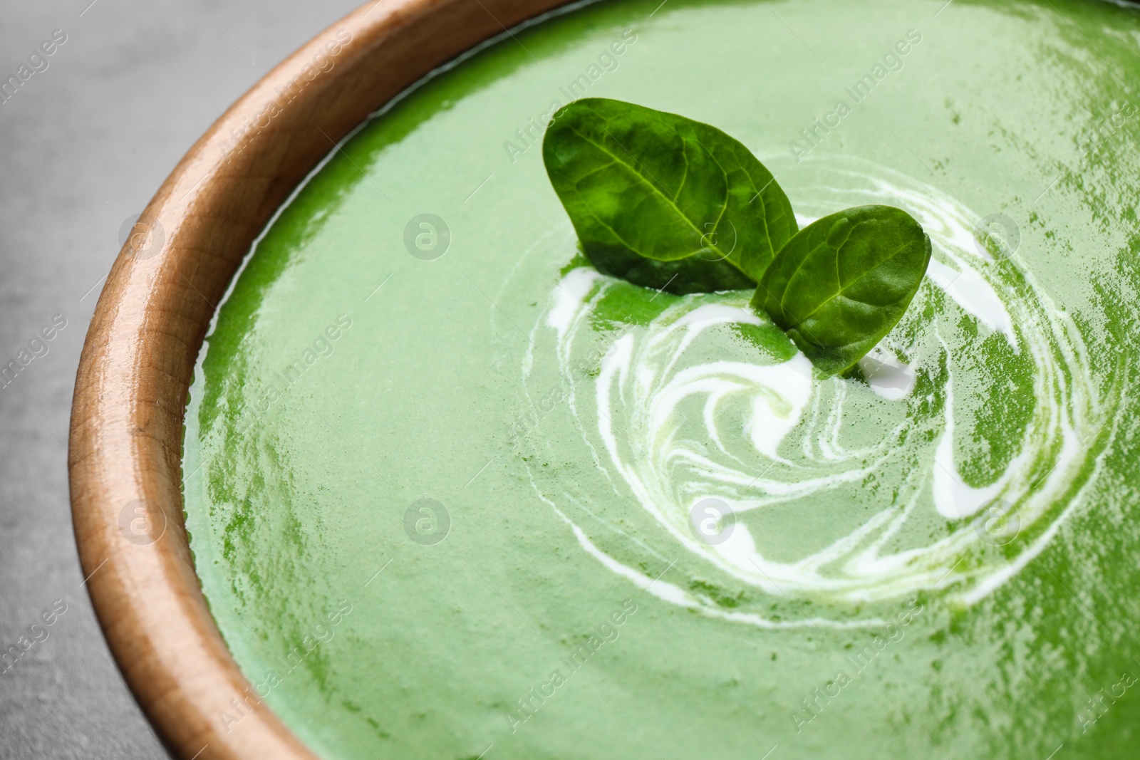 Photo of Bowl of healthy green soup with fresh spinach on grey table, closeup view