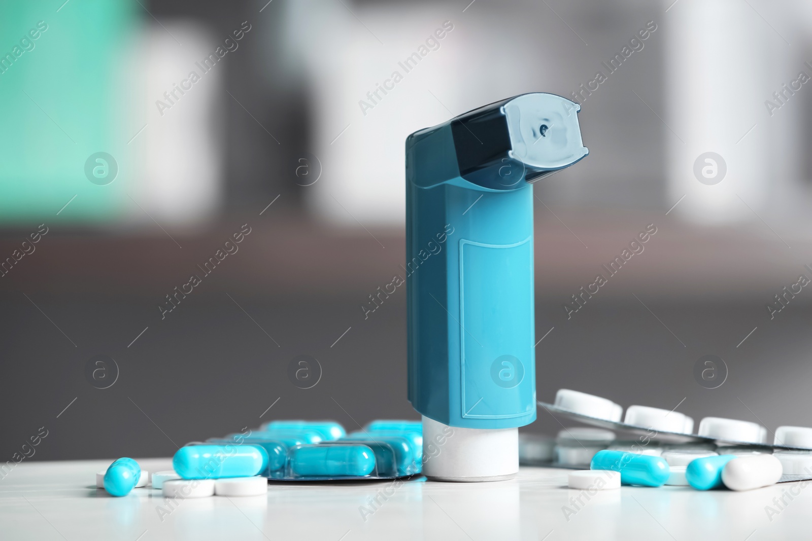 Photo of Asthma inhaler and pills on table against blurred background