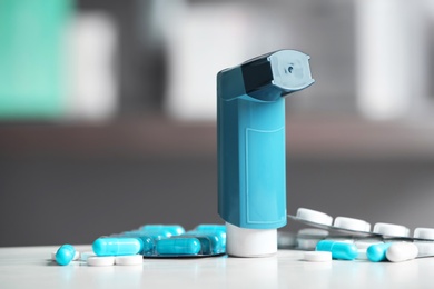 Asthma inhaler and pills on table against blurred background