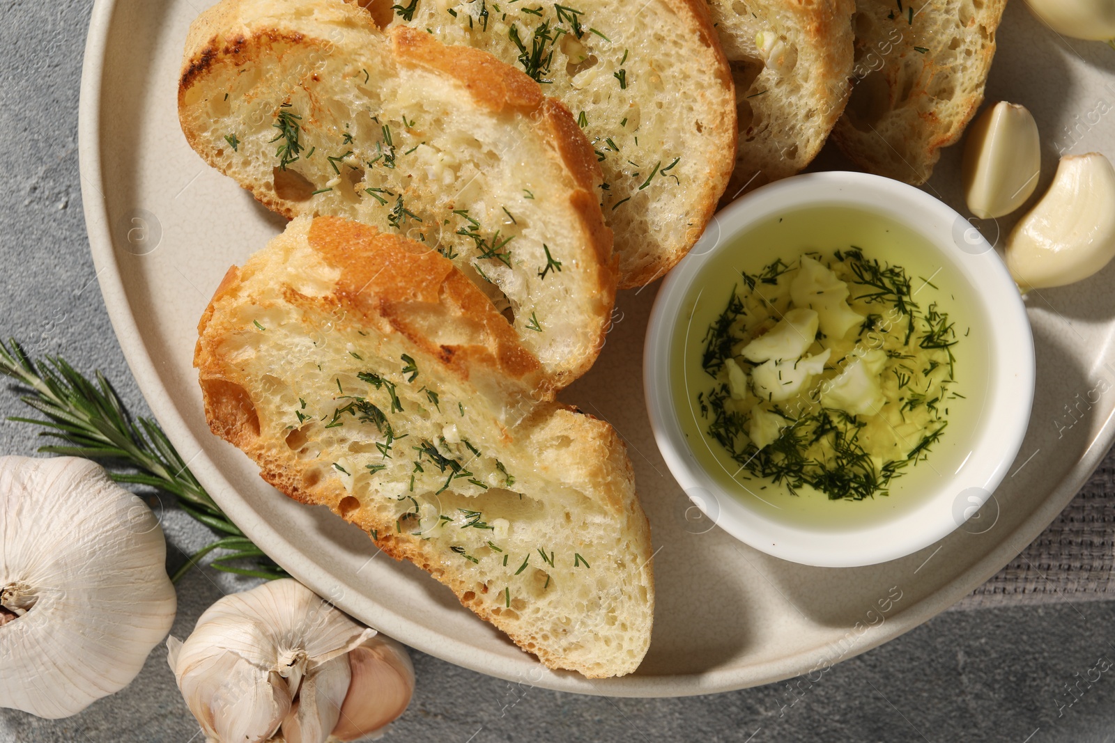 Photo of Tasty baguette with garlic and dill served on grey textured table, top view