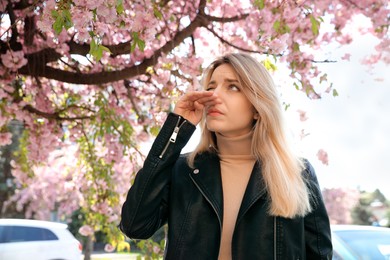 Photo of Woman suffering from seasonal pollen allergy near blossoming tree outdoors