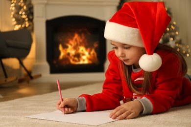 Photo of Cute child writing letter to Santa Claus while lying on floor at home, space for text. Christmas celebration
