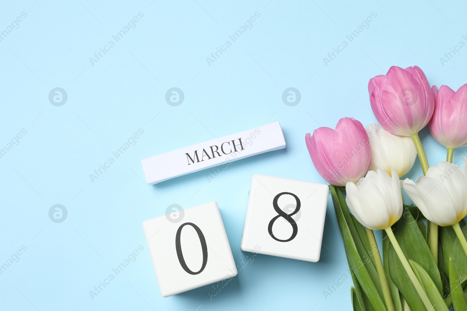 Photo of International Women's day - 8th of March. Wooden block calendar and beautiful flowers on light blue background, flat lay. Space for text