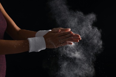 Photo of Young woman applying chalk powder on hands against dark background