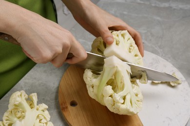 Woman cutting fresh cauliflower at light grey table, closeup