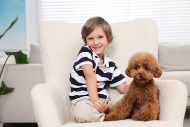 Little child with cute puppy in armchair at home. Lovely pet