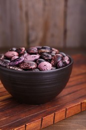 Photo of Bowl with dry kidney beans on wooden table, closeup