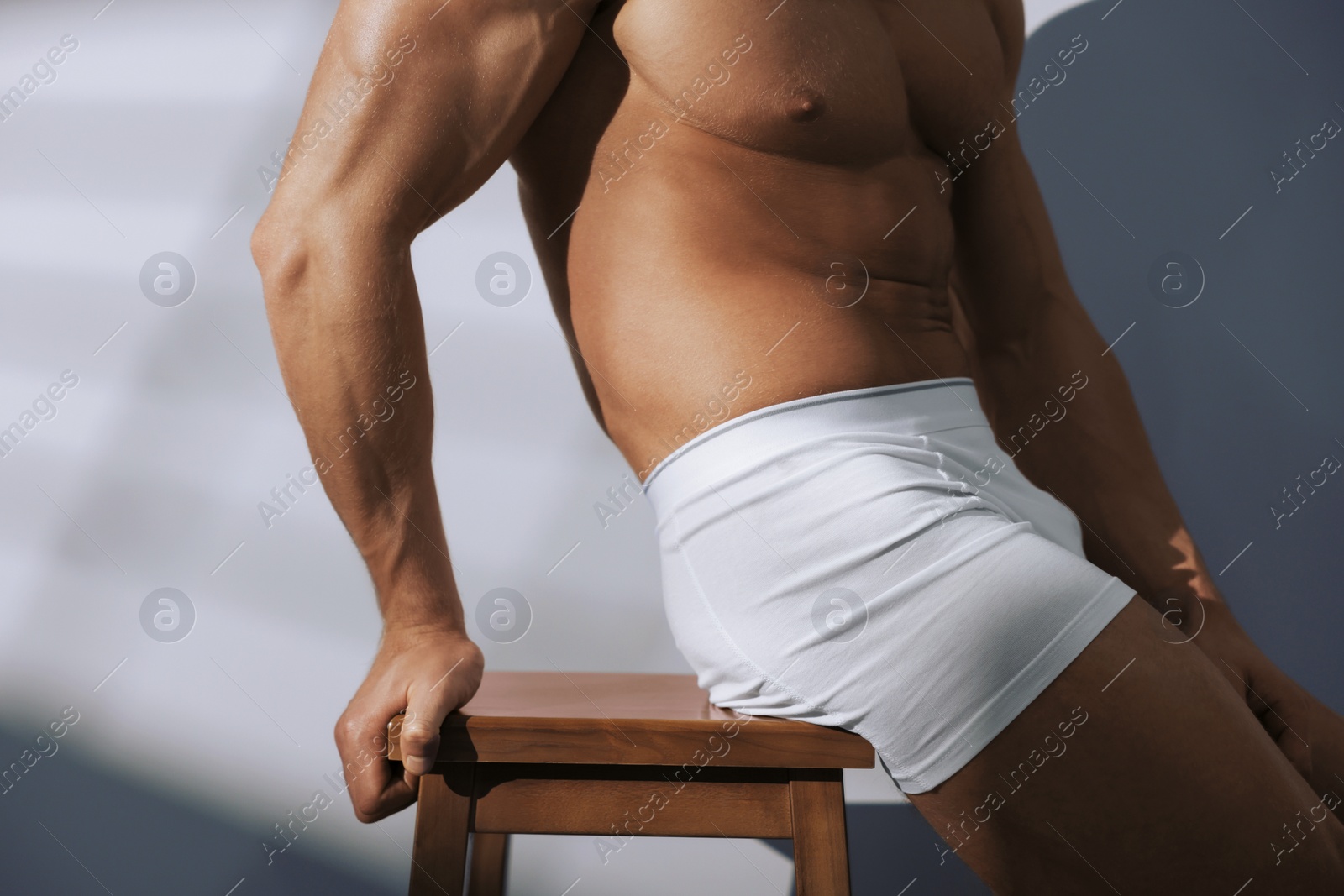 Photo of Young man in stylish white underwear sitting on chair near grey wall, closeup