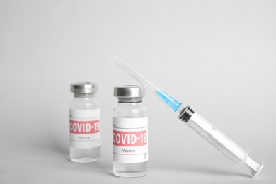 Vials with coronavirus vaccine and syringe on light background