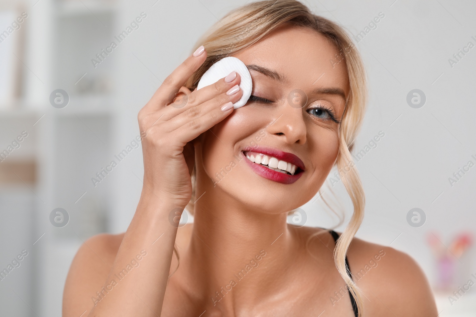 Photo of Smiling woman removing makeup with cotton pad indoors, closeup
