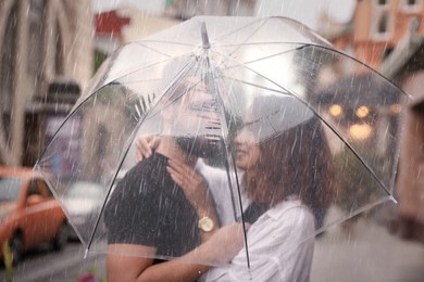 Young couple with umbrella enjoying time together under rain on city street