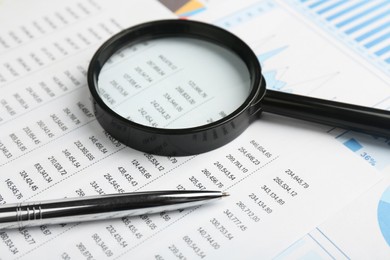 Photo of Magnifying glass and pen on accounting documents with data, closeup