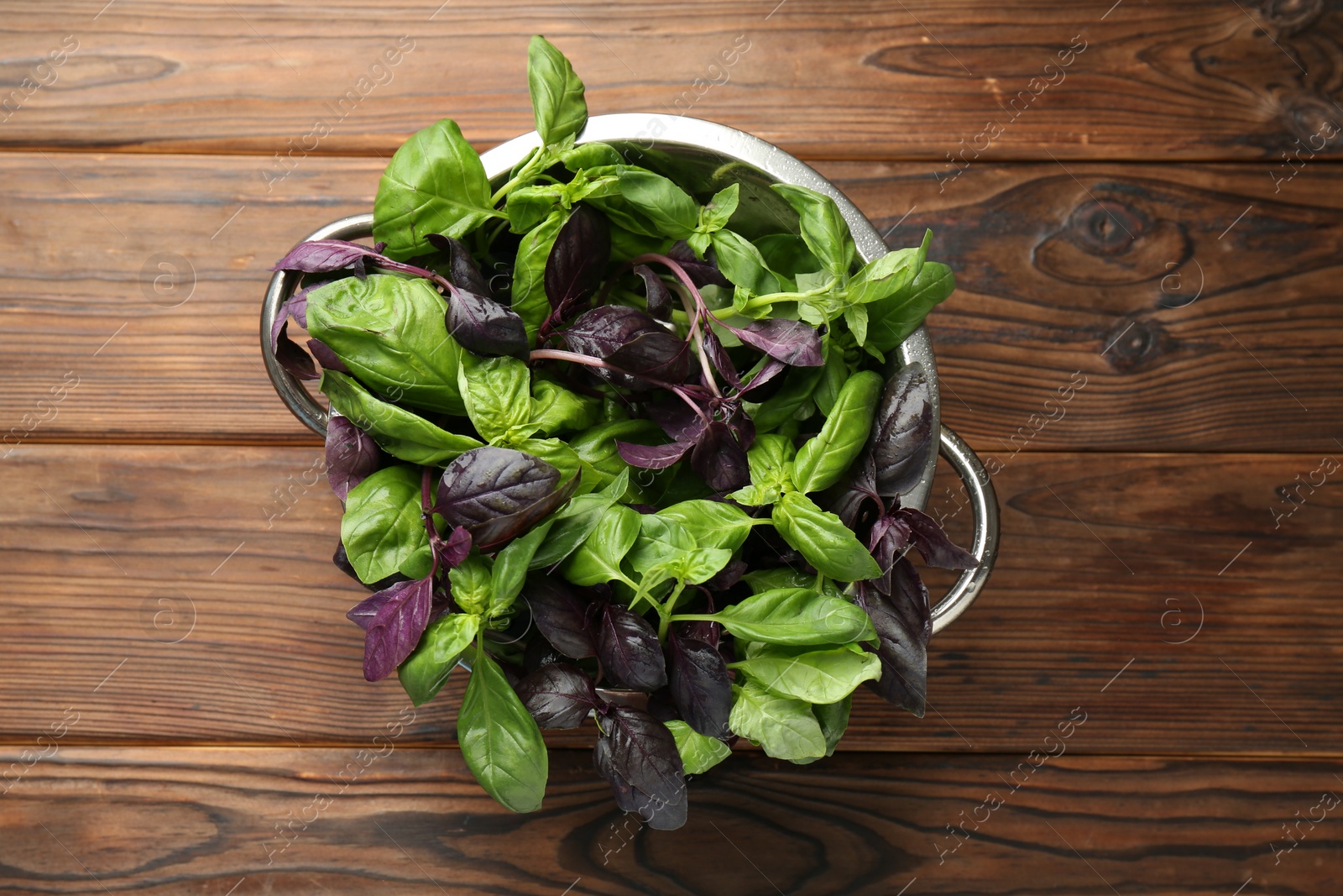 Photo of Metal colander with different fresh basil leaves on wooden table, top view