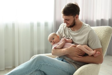 Father with his cute baby in armchair at home, space for text