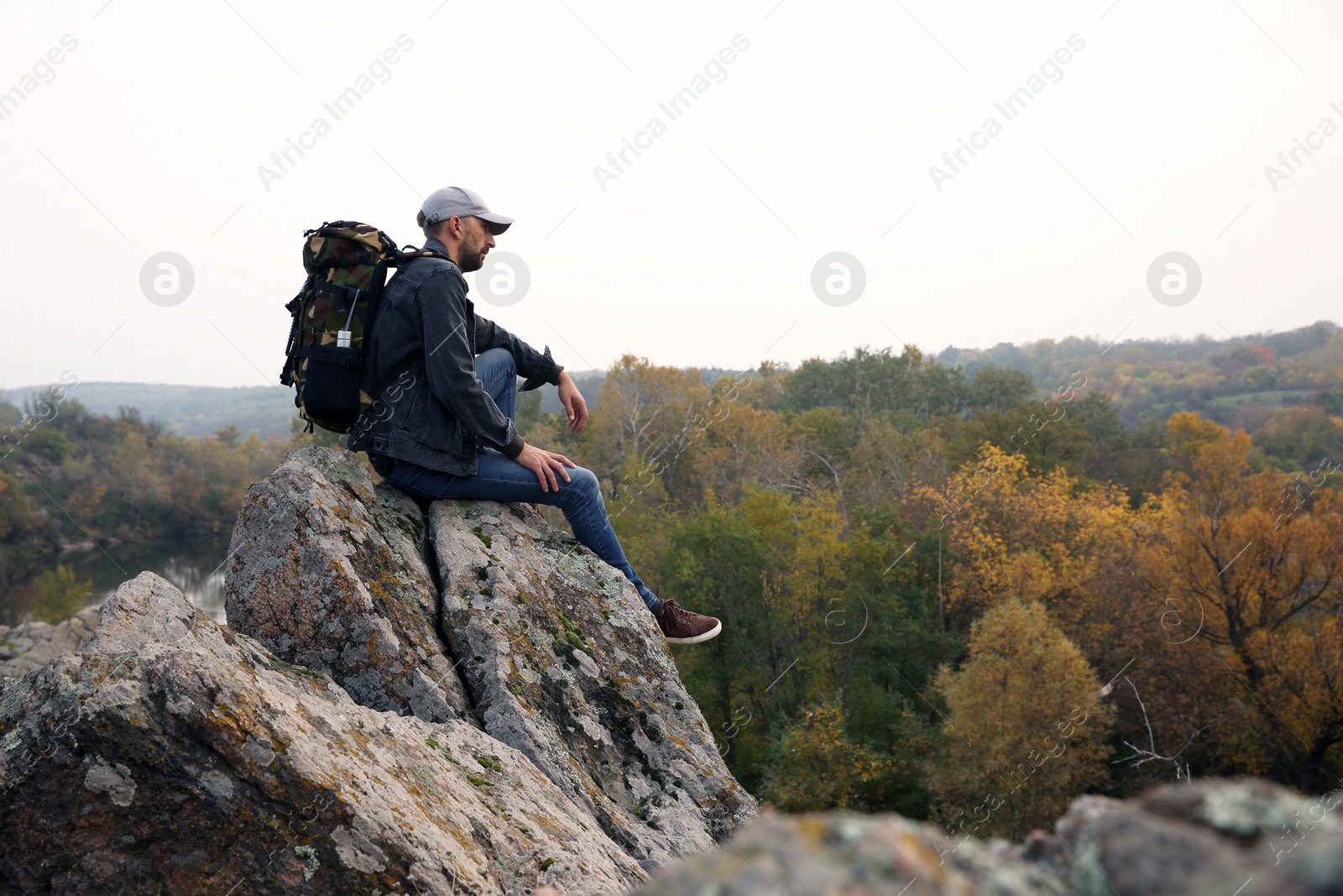 Photo of Hiker with travel backpack sitting on steep cliff on autumn day