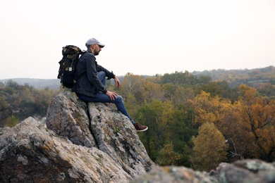 Photo of Hiker with travel backpack sitting on steep cliff on autumn day