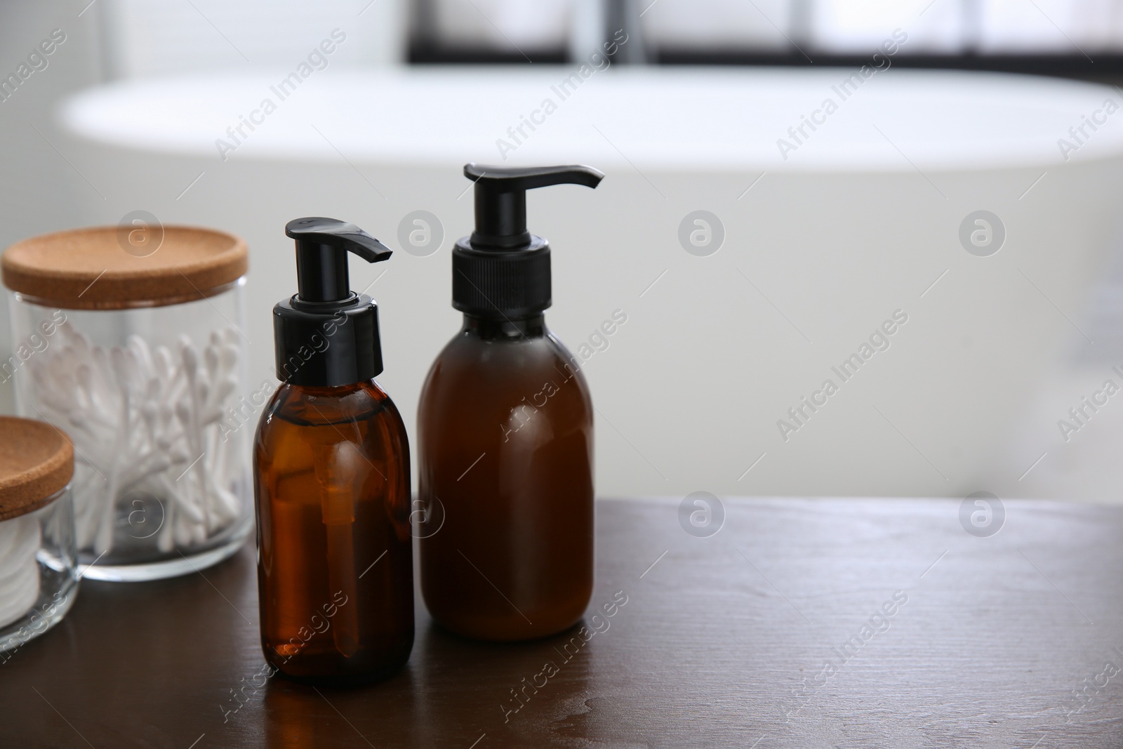 Photo of Dispensers of liquid soap on wooden table in bathroom. Space for text