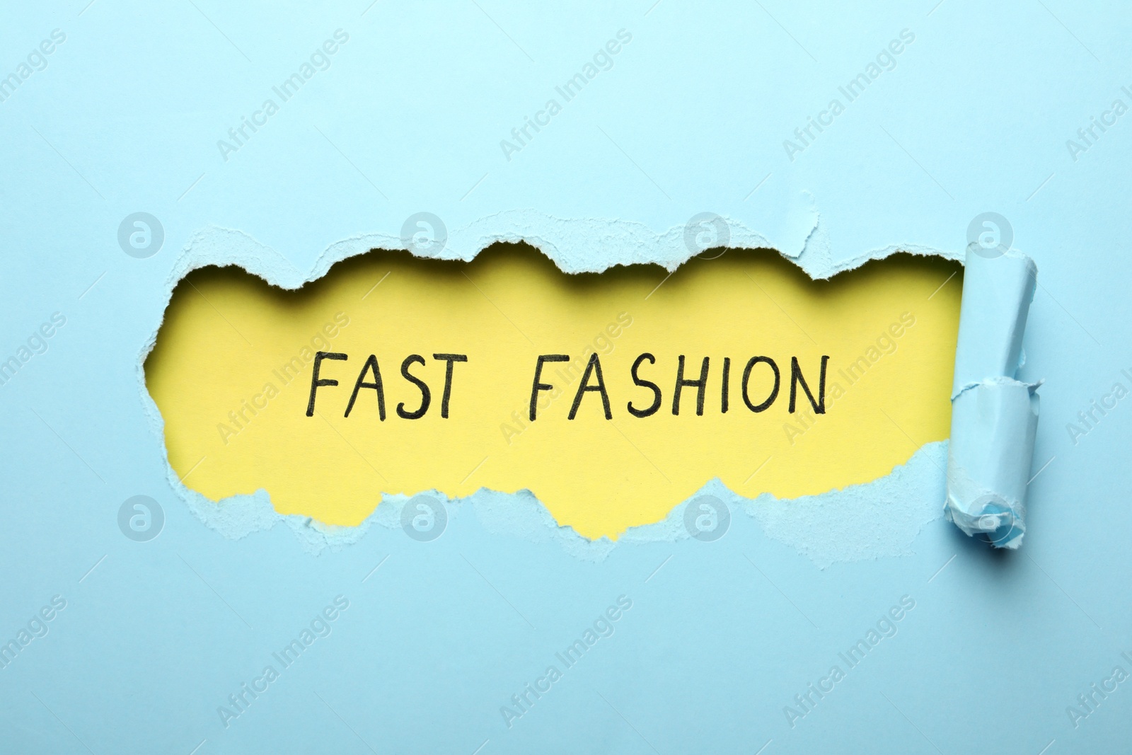 Photo of Phrase FAST FASHION written on yellow background, view through hole in light blue paper