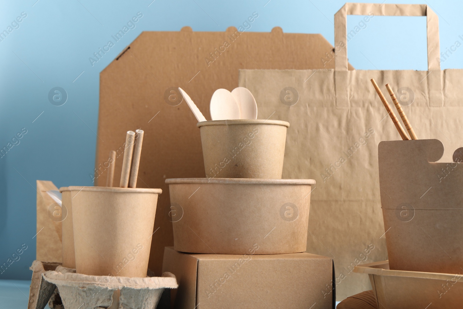 Photo of Eco friendly food packaging. Paper containers, tableware and bag on light blue background, closeup