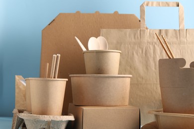 Photo of Eco friendly food packaging. Paper containers, tableware and bag on light blue background, closeup