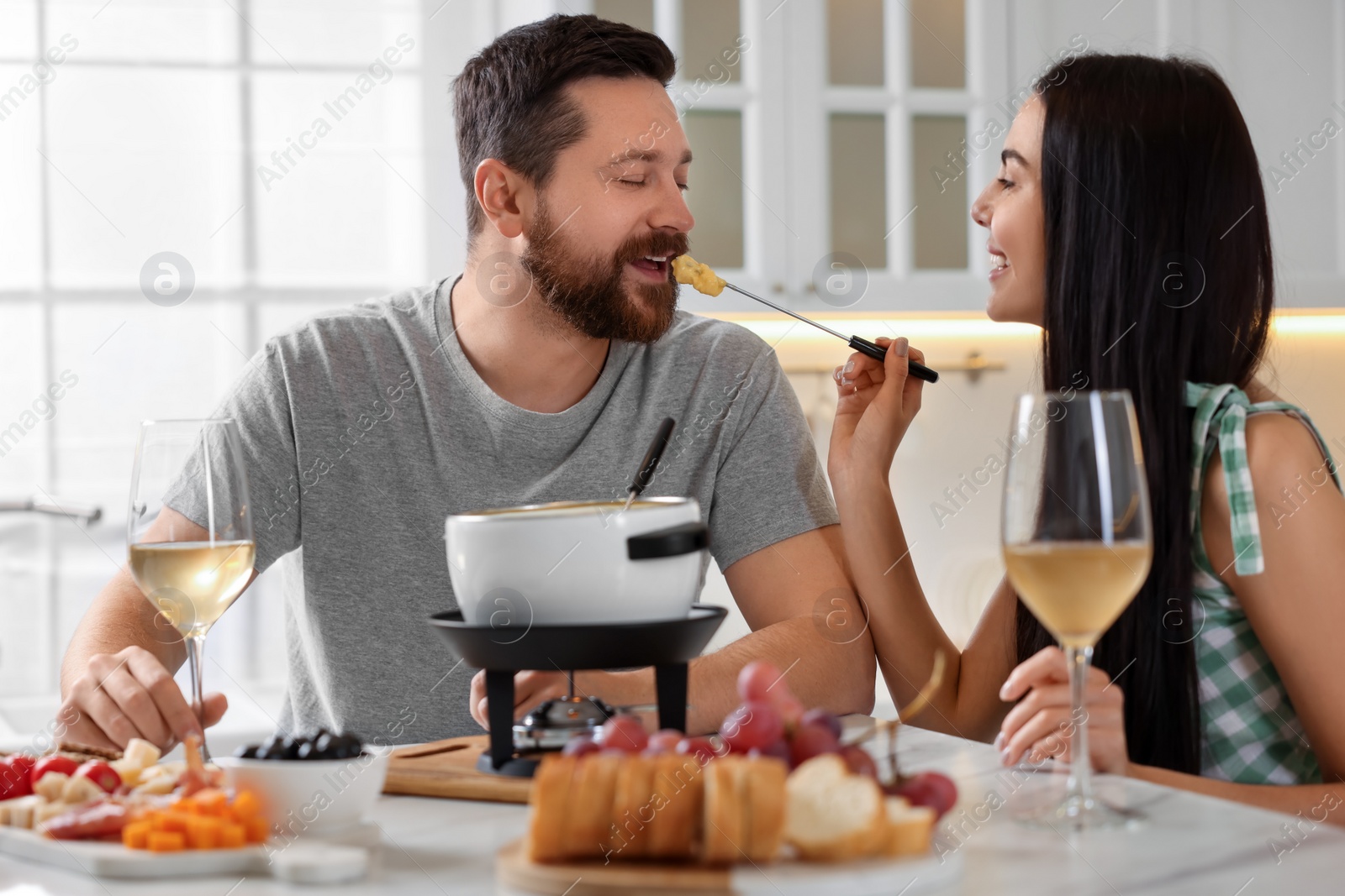 Photo of Affectionate couple enjoying cheese fondue during romantic date in kitchen