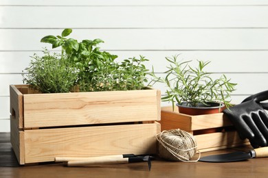 Photo of Crates with different potted herbs and gardening tools on wooden table